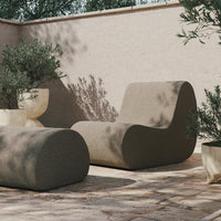 "Neutral beige lounge chair and ottoman with smooth curves, complemented by a rustic stone patio and greenery."