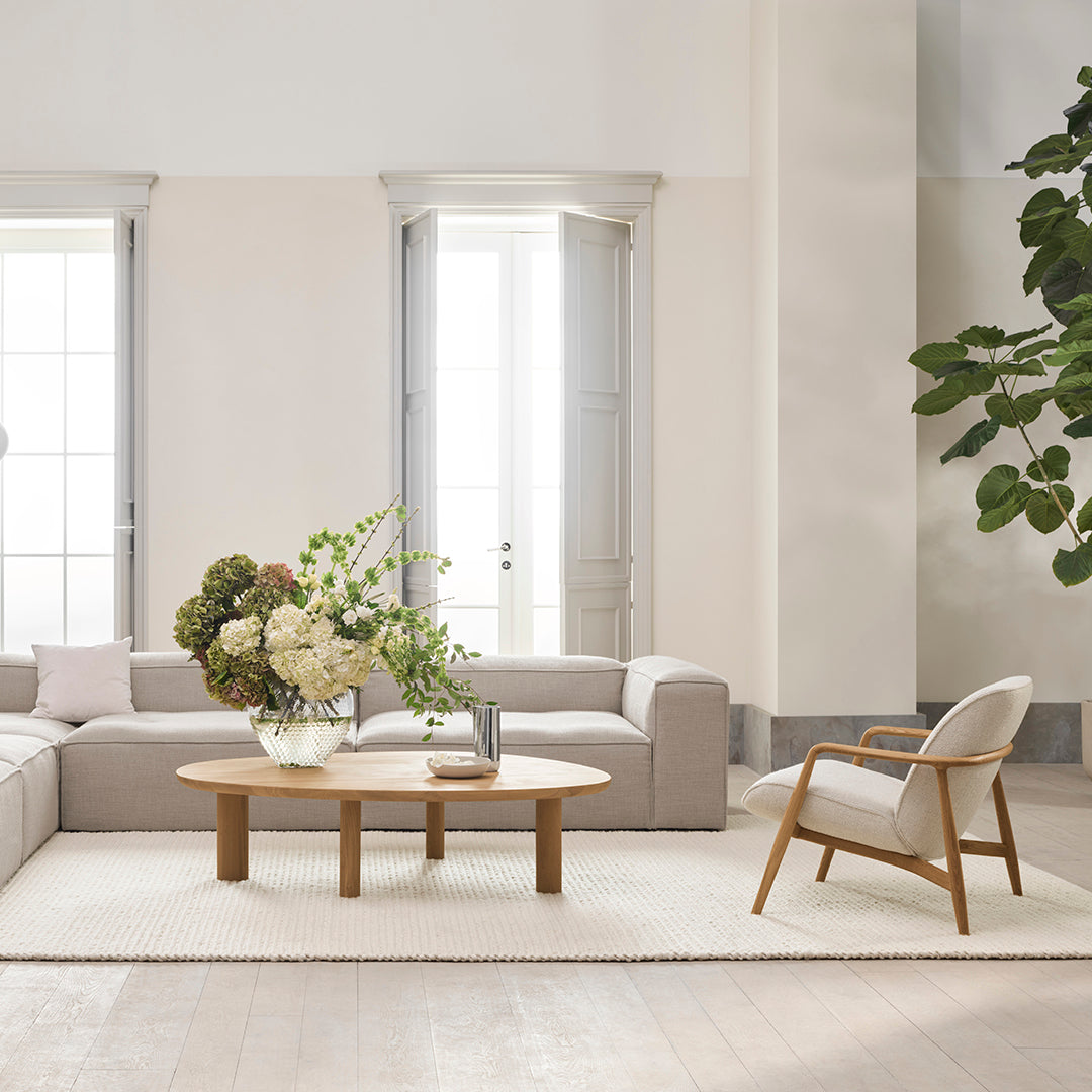 Cozy living room featuring soft beige sofa, light wood coffee table, and lush green plants, accented by neutral decor.