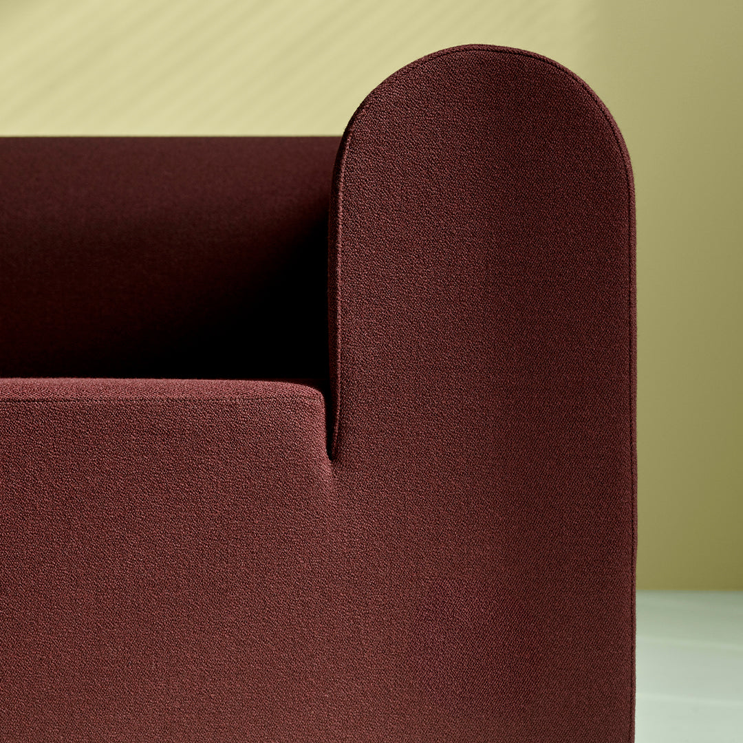Textured burgundy sofa detail against a soft yellow background, showcasing rich colors and modern design.