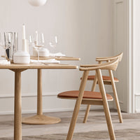 Minimalist wooden dining table with light beige accents, complemented by warm terracotta chair cushions and elegant glassware.