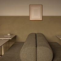 Gray cylindrical sofa on an olive-green wall with minimalist decor and framed artwork above.