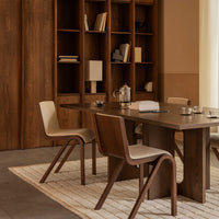 Modern wood dining table with beige and brown chairs, paired with a textured neutral rug and warm-toned wood shelves.