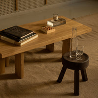 "Natural wood coffee table with a dark wooden stool, featuring a neutral beige rug and subtle decorative elements."
