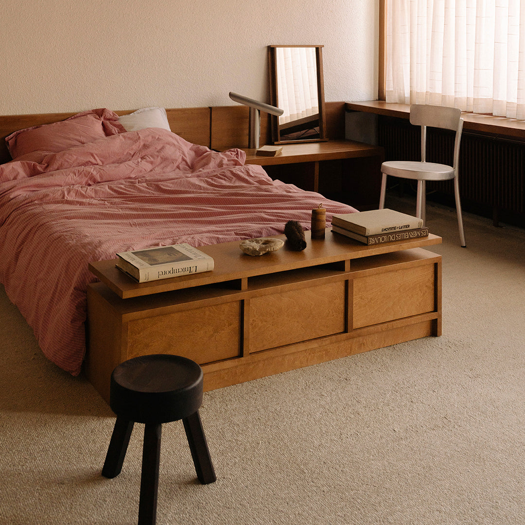 Cozy bedroom featuring a soft pink bedding set, wooden furniture, and neutral-toned accents in a warm, inviting space.