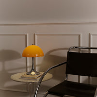 Glossy black chair beside a clear table, featuring a vibrant yellow dome lamp against a neutral wall.