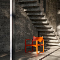 Vibrant orange chair with bold geometric design in a modern concrete setting. Natural light enhances colors.