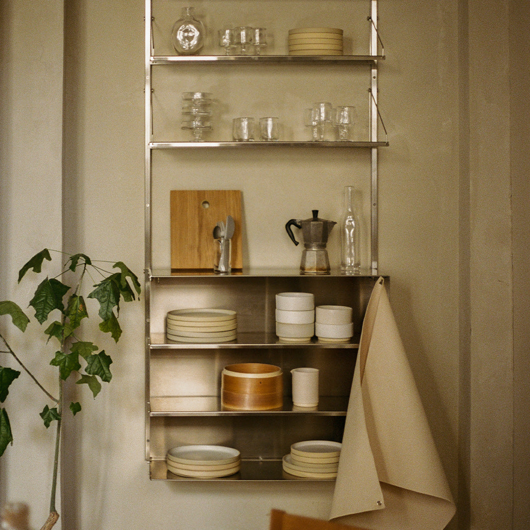 "Metal shelving with white, beige, and wooden dishware; glassware adds sparkle against muted backdrop."