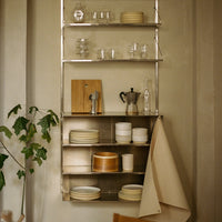 "Metal shelving with white, beige, and wooden dishware; glassware adds sparkle against muted backdrop."