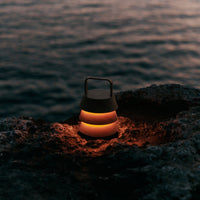"Portable lantern with a sleek black and warm orange glow, set against a dark rocky shoreline."