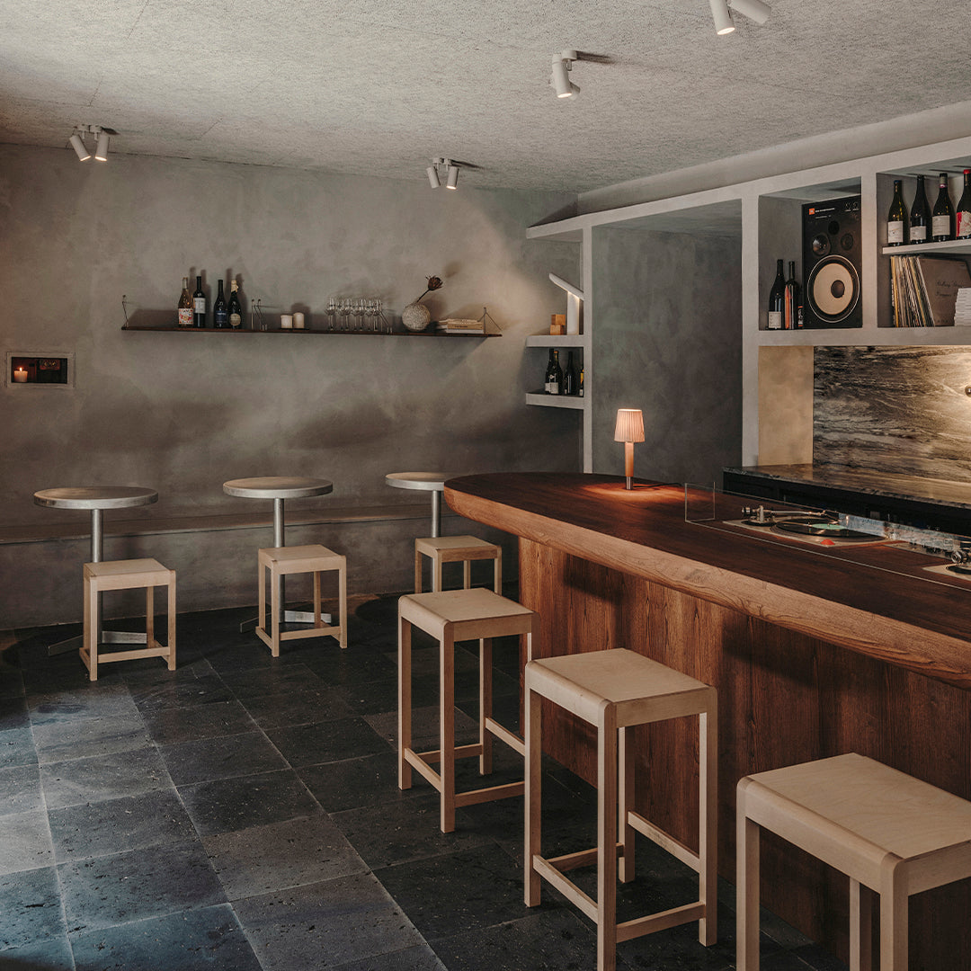 "Modern bar setting featuring dark gray stone flooring, light wood accents, and warm metallic lighting."