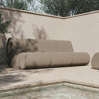 Modern beige sofa with minimalist design, featuring a smooth texture and rounded shapes, set against a natural backdrop.