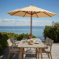 Yellow and white striped patio umbrella over a wooden table by the water, surrounded by greenery.