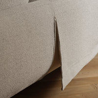 Beige textured fabric with a subtle pattern, showcasing a tailored edge detail on a sofa.
