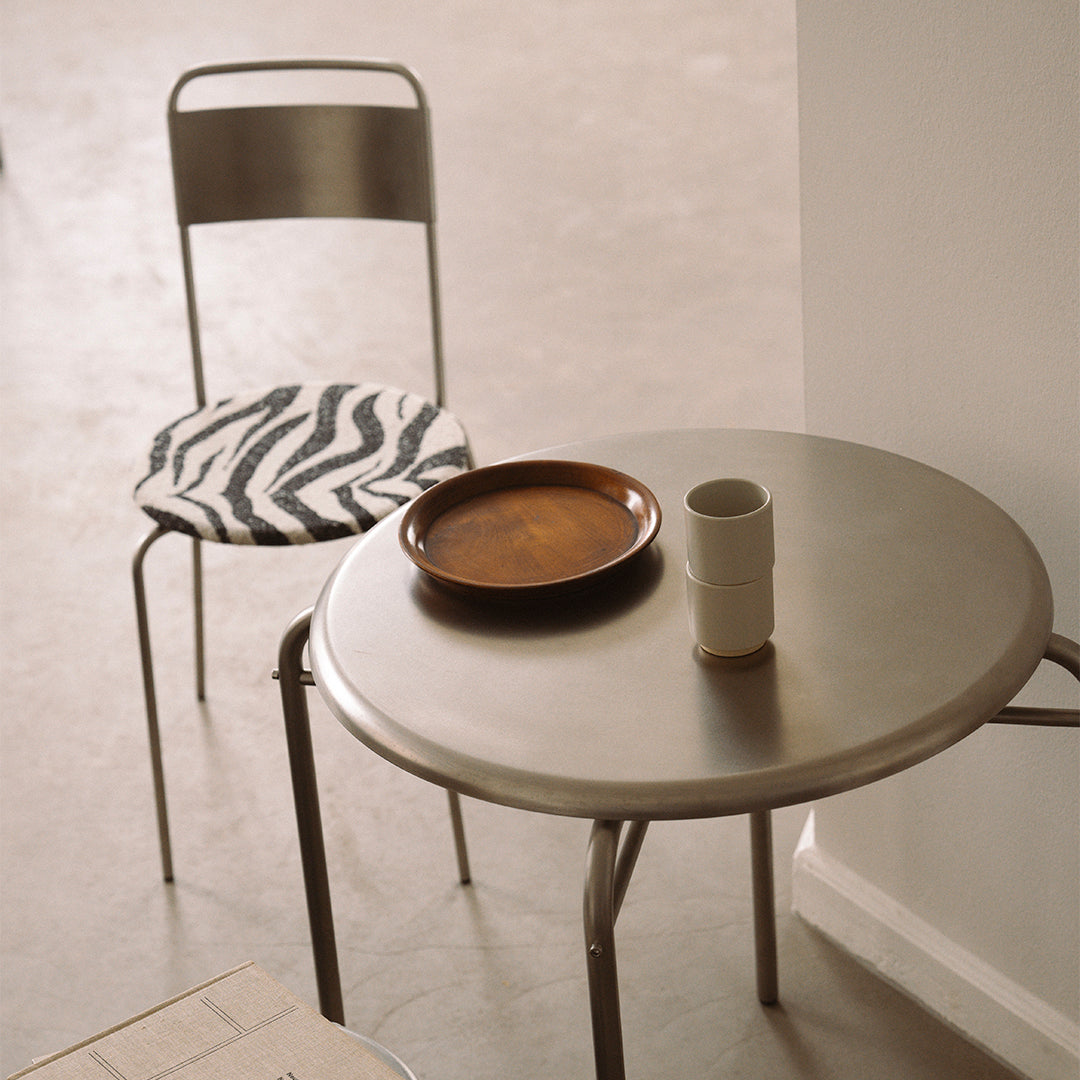 Metal table with a circular design, featuring a striped black and white chair cushion and earthy brown plate.