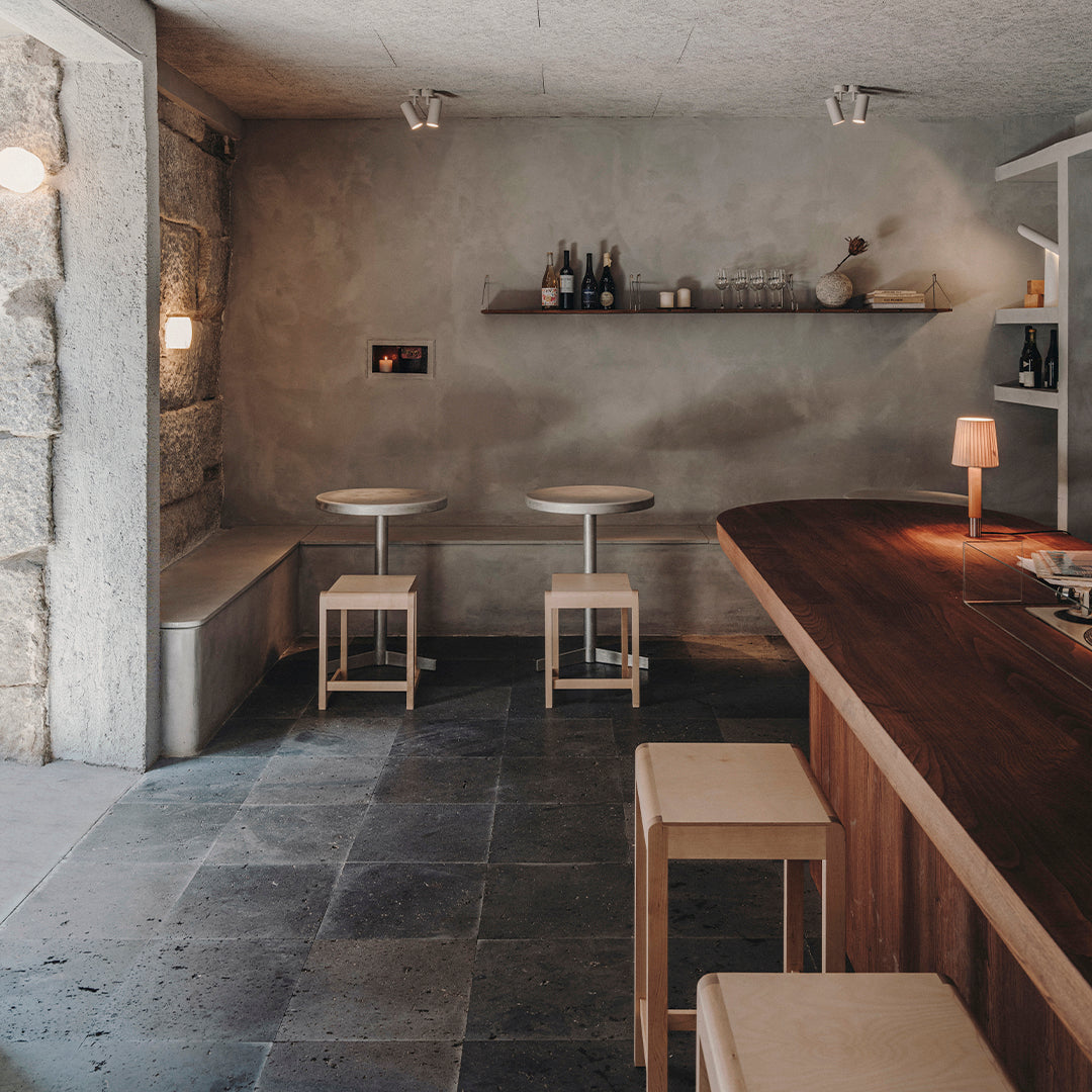 Neutral gray walls, wood accents, and minimalist design create a cozy, modern bar ambiance with soft lighting.