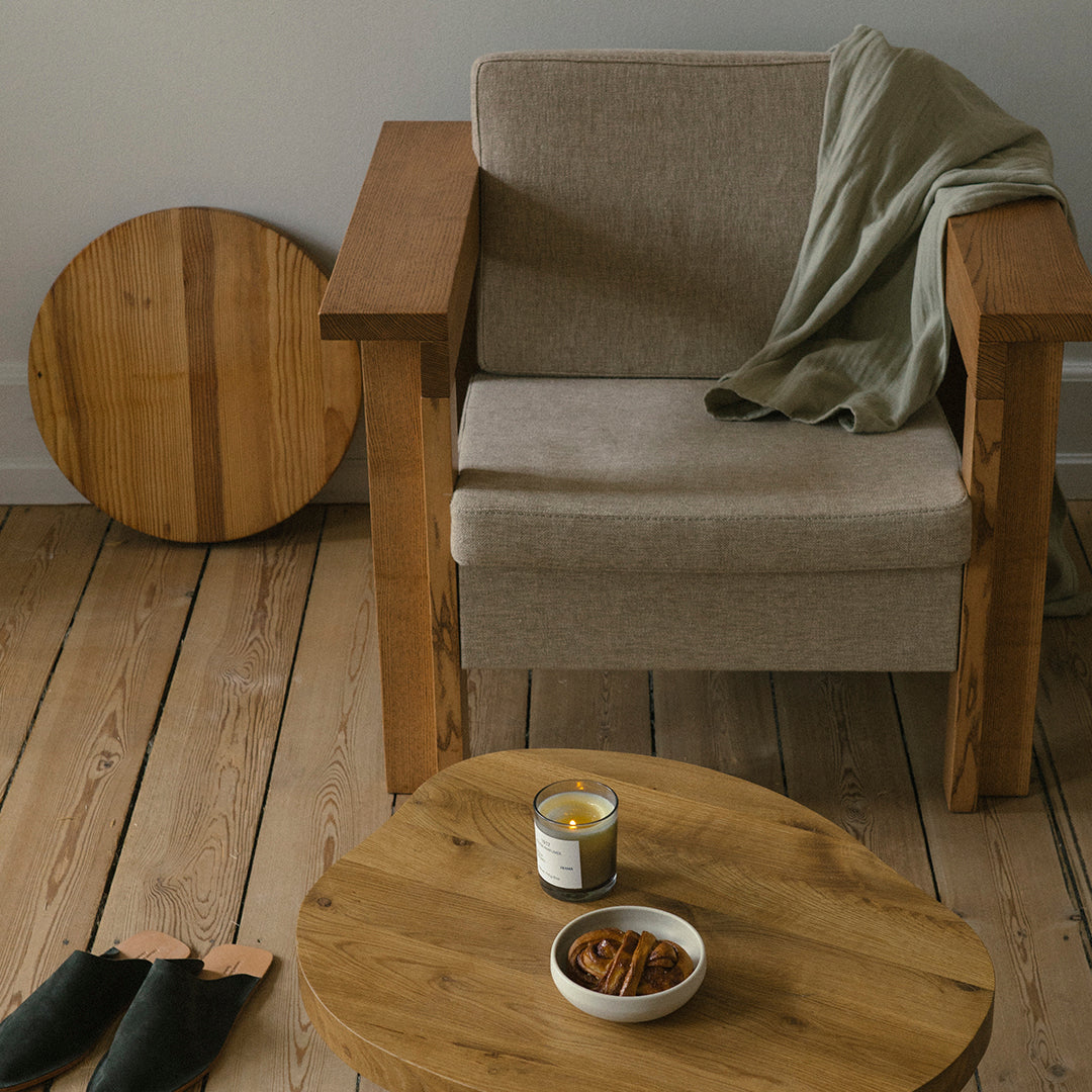 Natural wood tones with beige upholstery and a soft green throw, accented by round wooden table and coasters.