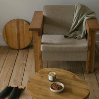 Natural wood tones with beige upholstery and a soft green throw, accented by round wooden table and coasters.