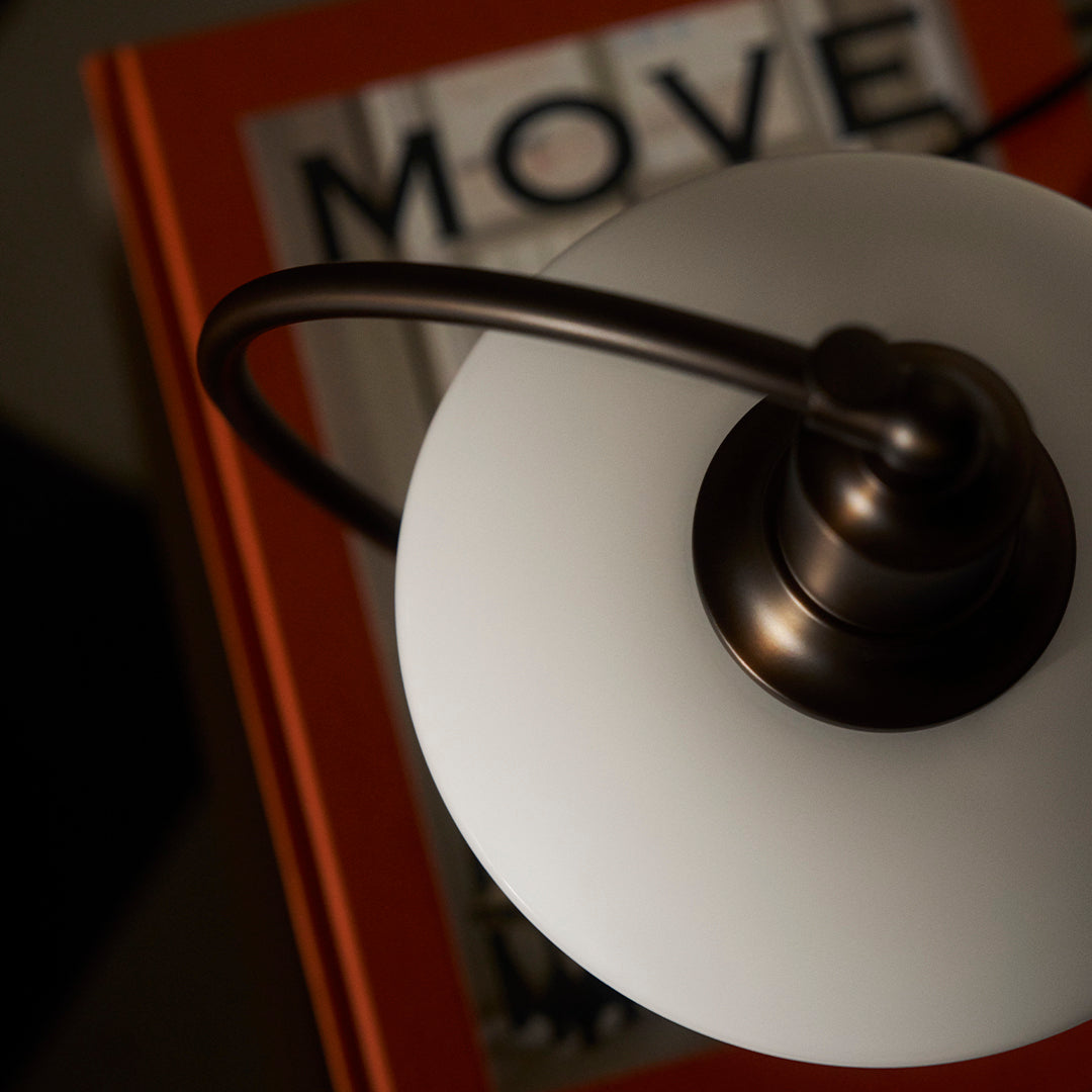 White glass lamp shade with bronze accents, resting above a vibrant orange book cover featuring the word "MOVE."