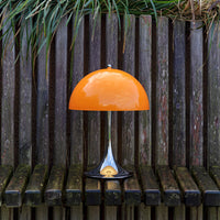 Orange dome lamp with a sleek silver base, set against a rustic wooden background. Modern and vibrant design.