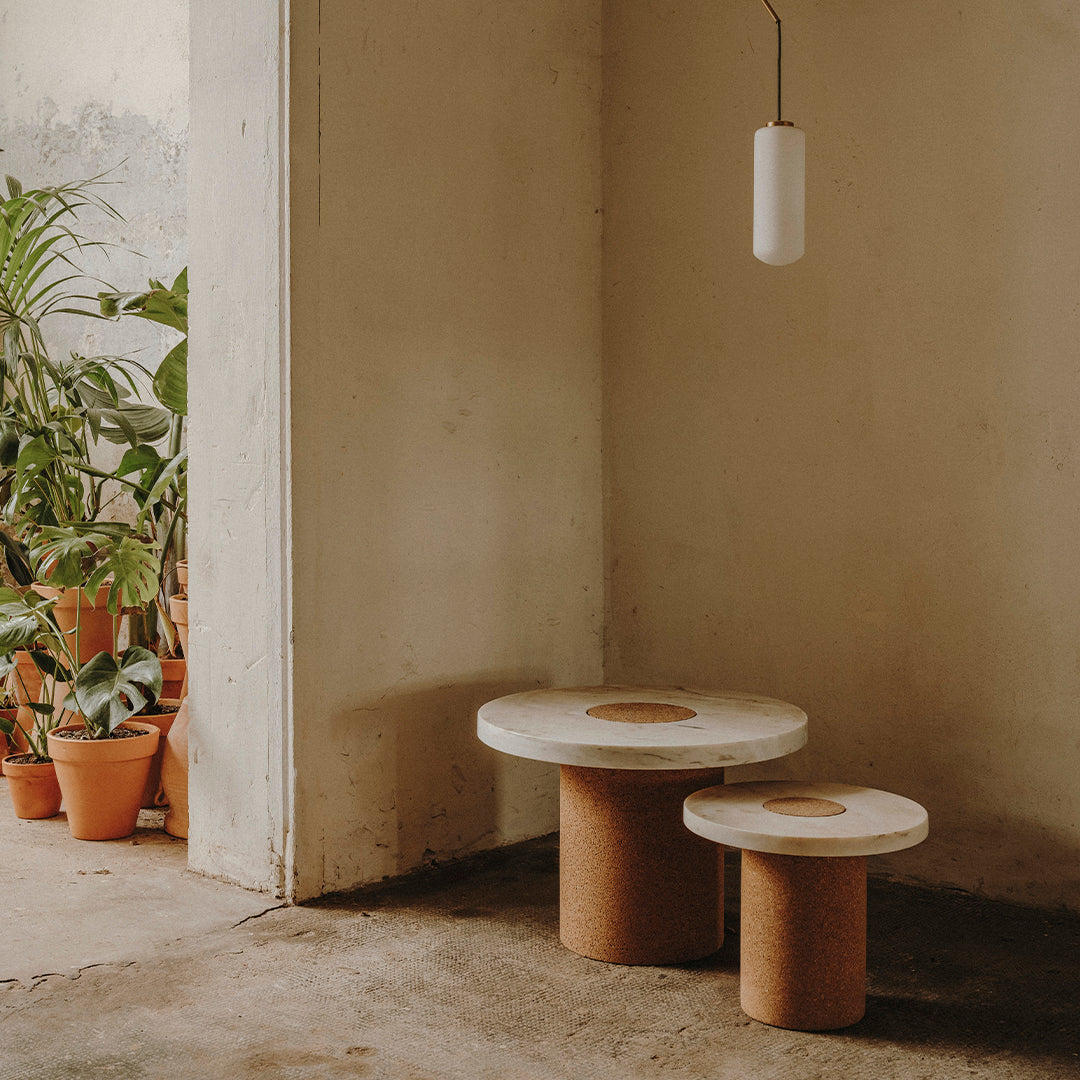 Two modern side tables with circular white tops and natural cork bases, set against a muted, earthy backdrop.