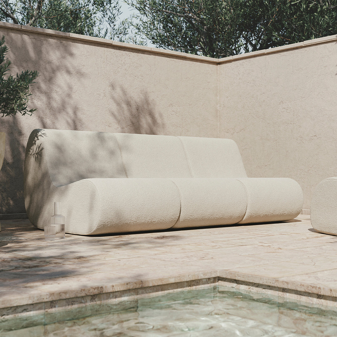 Beige modern sofa with smooth, rounded lines against a neutral stone backdrop, perfect for contemporary outdoor spaces.
