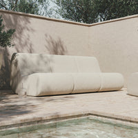 Beige modern sofa with smooth, rounded lines against a neutral stone backdrop, perfect for contemporary outdoor spaces.