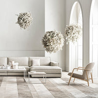 Light beige sofa in a minimalist room with white walls, patterned wooden floor, and hanging white floral arrangements.