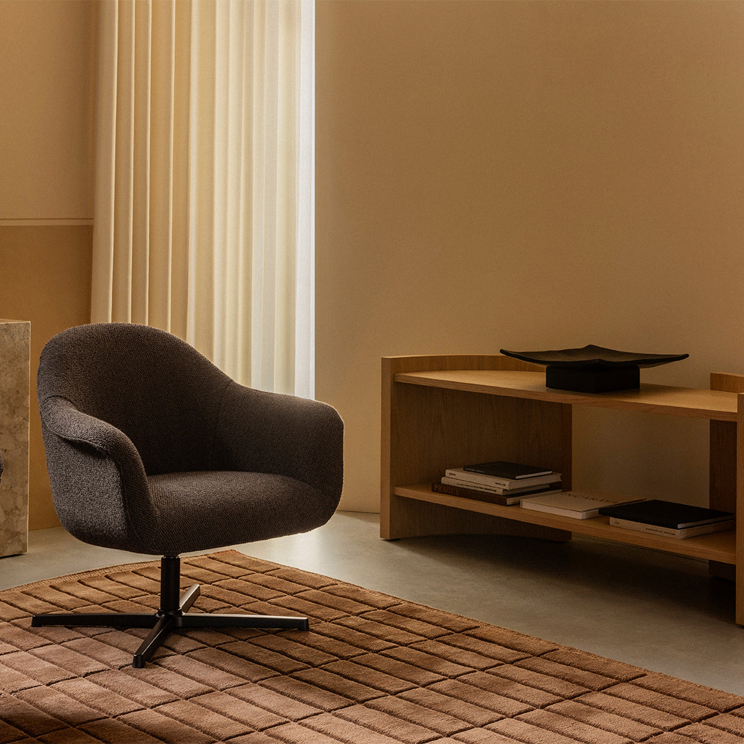 Stylish dark gray upholstered chair on a brown textured rug, complemented by soft beige walls and light curtains.