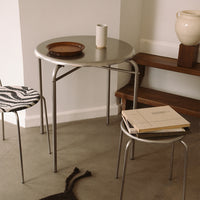"Round metallic table with sleek gray surface; one chair features black and white zebra print design."