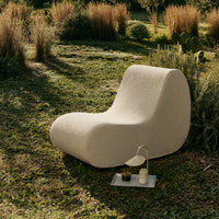 Curved cream lounge chair on grass, featuring a smooth textured surface and minimalistic design.