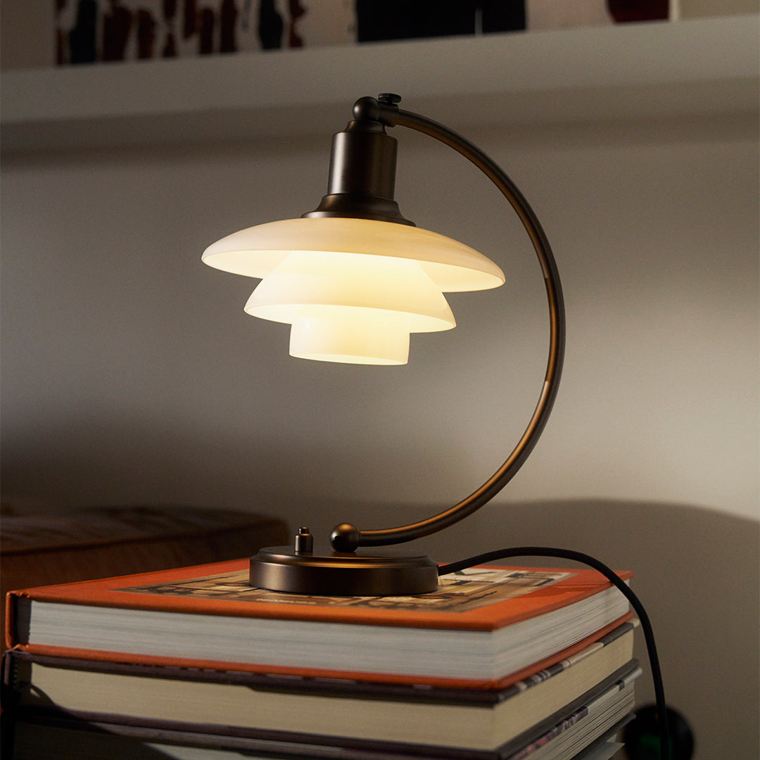 Modern bronze lamp with layered white glass shades, illuminating a warm ambiance on a stacked book arrangement.