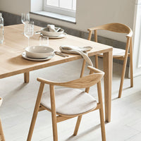 Natural wood tones with neutral beige seat cushions, minimalist dining setup featuring elegant tableware and glassware.