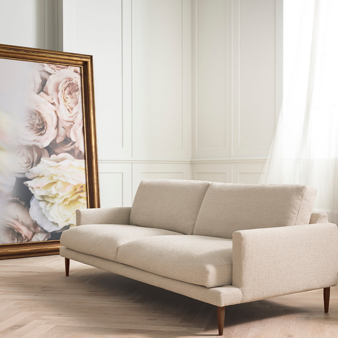Beige fabric sofa with wood legs, paired with a large floral artwork featuring soft pink and cream hues.