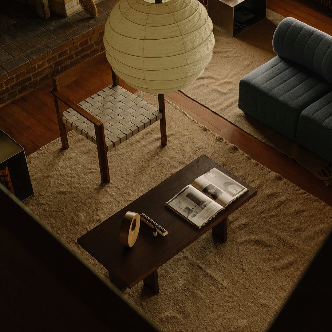 Warm wood tones of a coffee table with a textured beige rug, complemented by a soft blue sofa and a round white lantern.