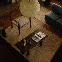 Warm wood tones of a coffee table with a textured beige rug, complemented by a soft blue sofa and a round white lantern.