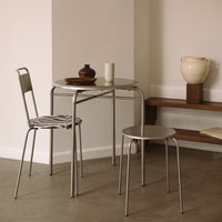 Round metallic table with a silver chair featuring a striped cushion, set against neutral-toned walls and decor.
