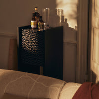 Black cabinet with intricate geometric pattern, accented by warm light and natural tones from surrounding decor.