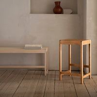 Light wooden furniture set with soft, natural tones against a minimalist beige wall and rustic wooden floor.