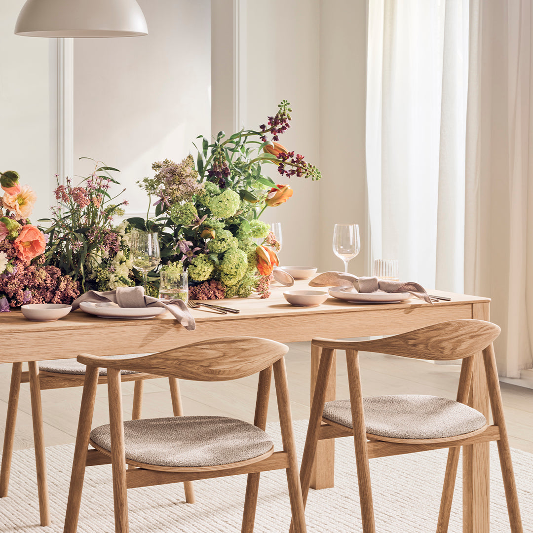 "Elegant dining table set with a floral centerpiece featuring vibrant colors and soft textures in a light, airy room."