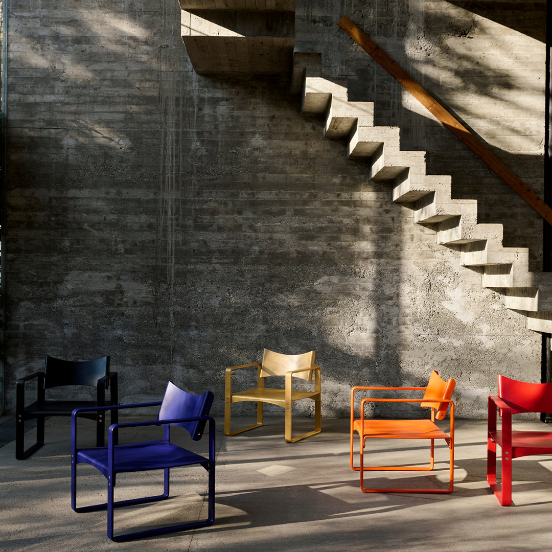Colorful modern chairs in black, blue, yellow, orange, and red displayed against a concrete backdrop and patterned stairs.