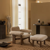 Beige textured armchair and ottoman on a natural brick-patterned rug in a warm-toned interior.