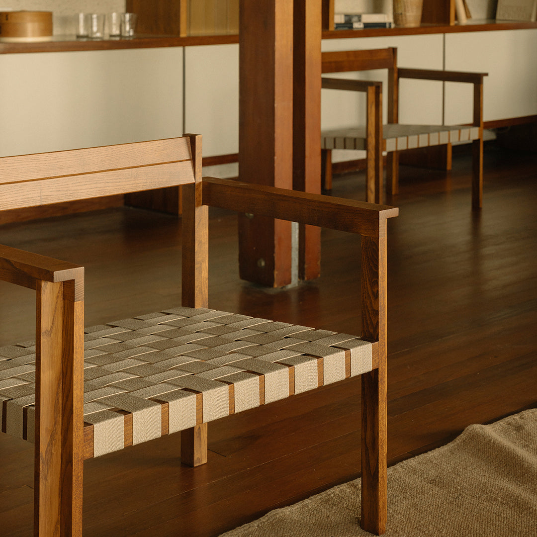 Wooden chair with a beige and white woven seat, set against a warm wood floor and neutral decor.