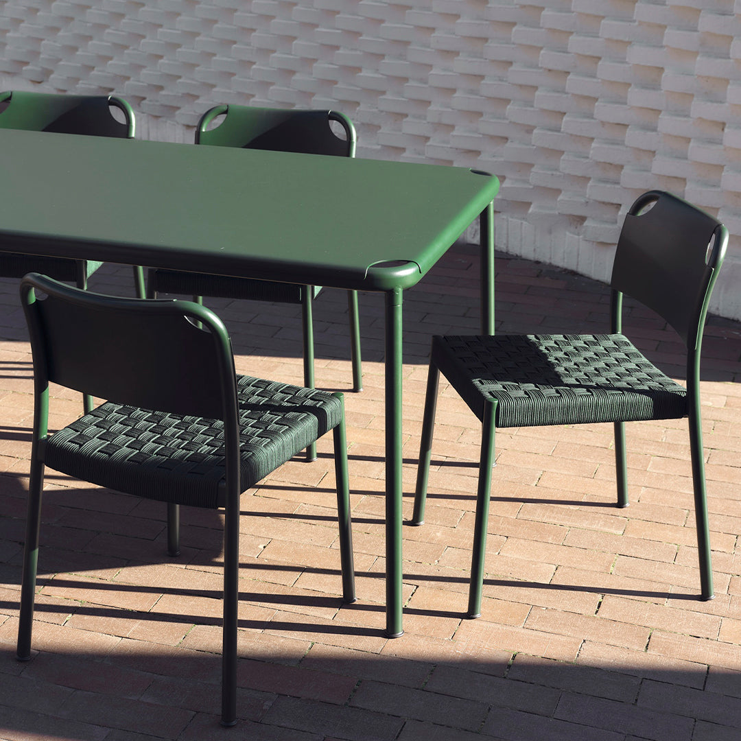 Green rectangular table with black woven pattern chairs, set against a textured light background.