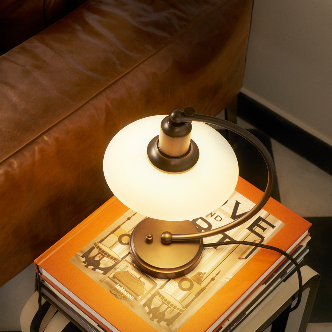 Modern table lamp featuring a round frosted glass shade and a sleek bronze base, set on colorful books.