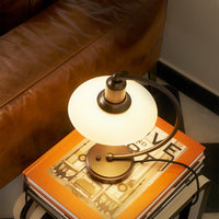 Modern table lamp featuring a round frosted glass shade and a sleek bronze base, set on colorful books.