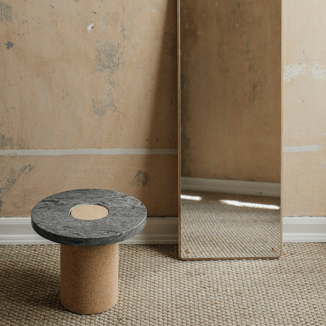 Gray marble-top round table with a cork base, set against a textured beige wall and a reflective mirror.