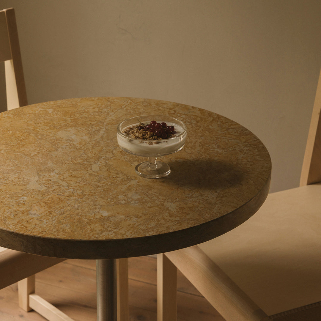 Round table with a warm, golden-brown marble pattern, paired with light-colored wooden chairs.