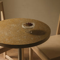 Round table with a warm, golden-brown marble pattern, paired with light-colored wooden chairs.