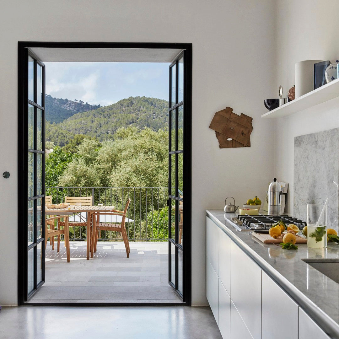 Bright white walls with sleek gray countertops, framed by a natural green outdoor view and black door accents.