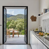 Bright white walls with sleek gray countertops, framed by a natural green outdoor view and black door accents.